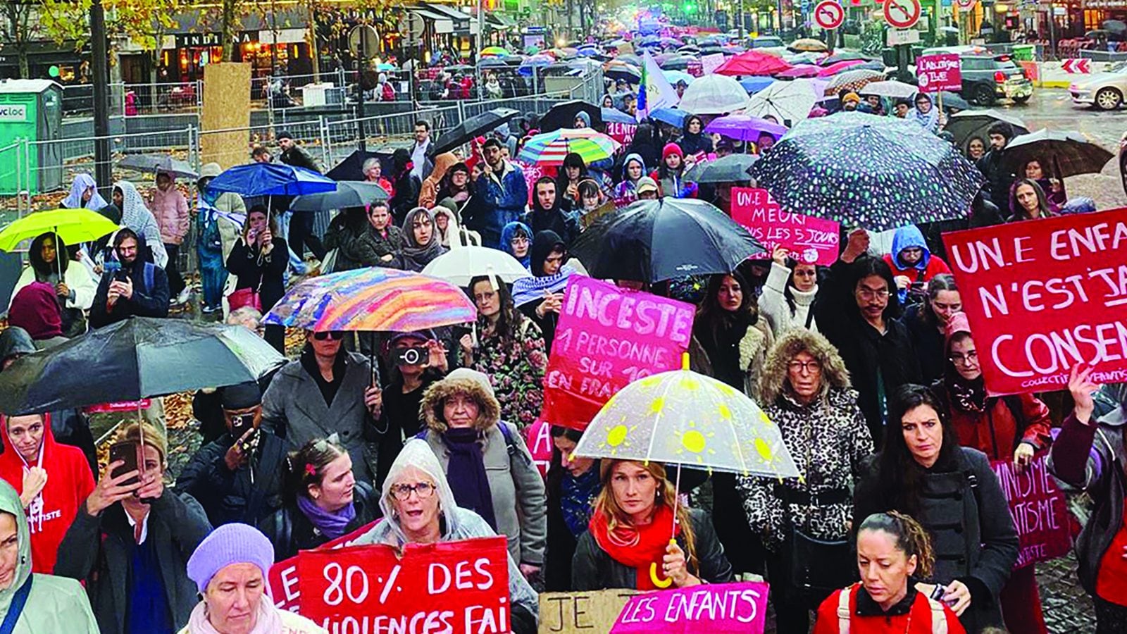 Une foule sous les parapluies dans une rue de Paris, pancartes rouges et roses levées : « Inceste : 1 personne sur 10 en France », « Un·e enfant n'est jamais consentant·e », « 80 % des violences faites… ».